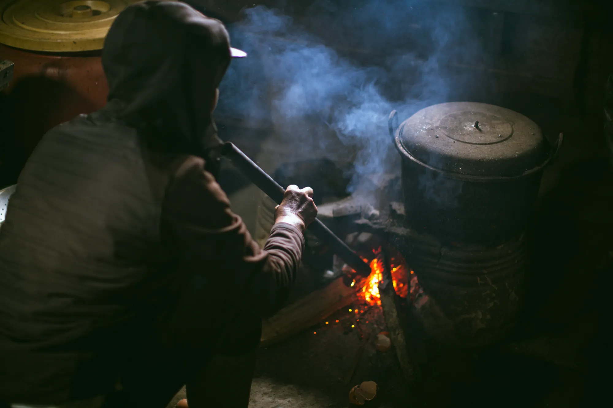 Waking the cooking fire with a bamboo blowpipe under a blackened pot