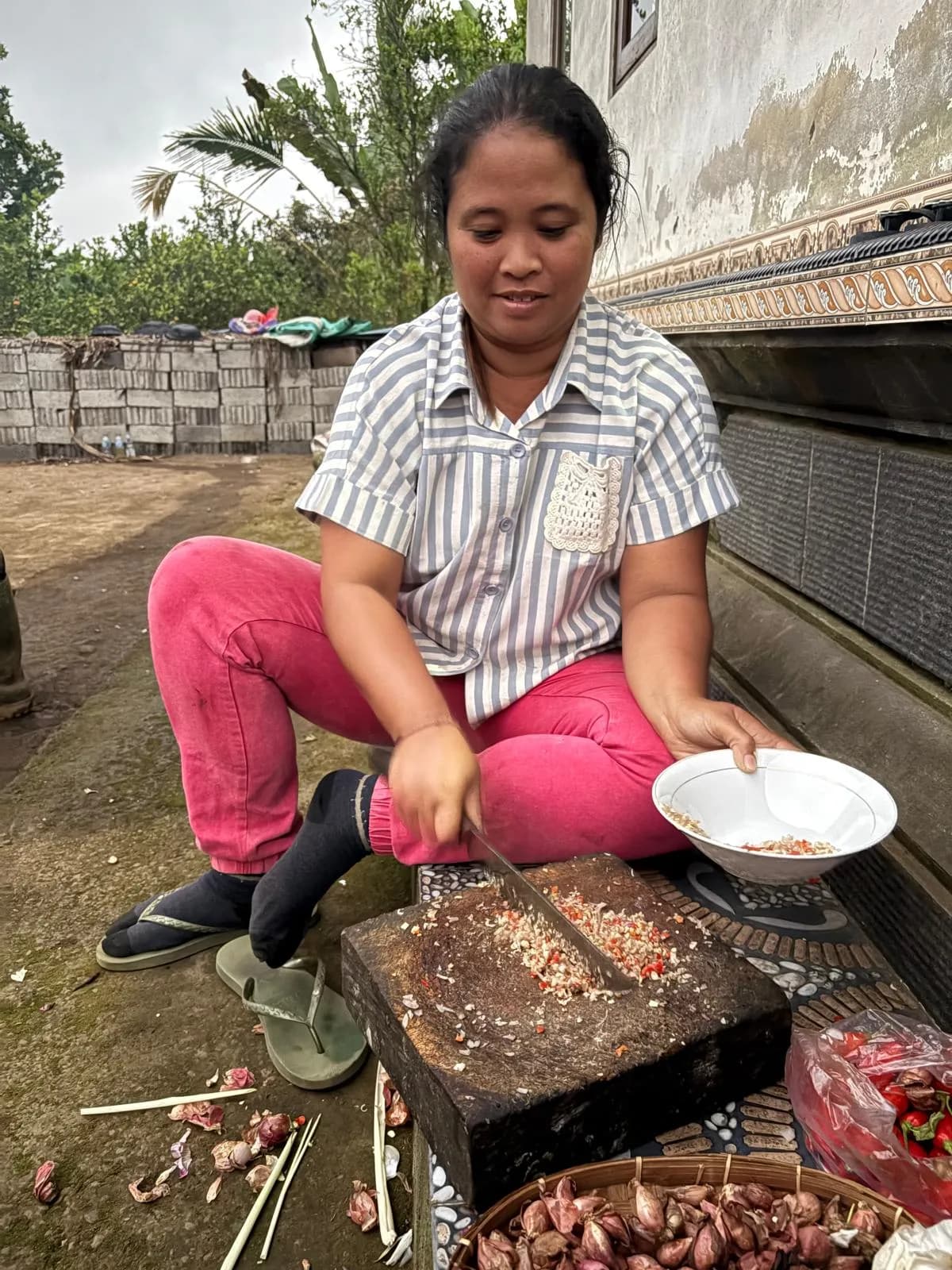 Chopping chillies and shallots into spice paste on the stone block in the yard